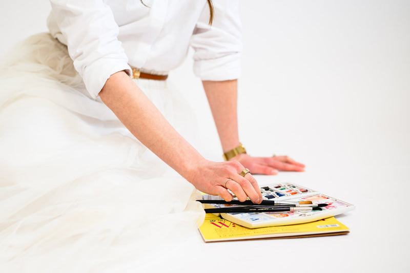Person sitting on the ground with watercolors and paintbrushes